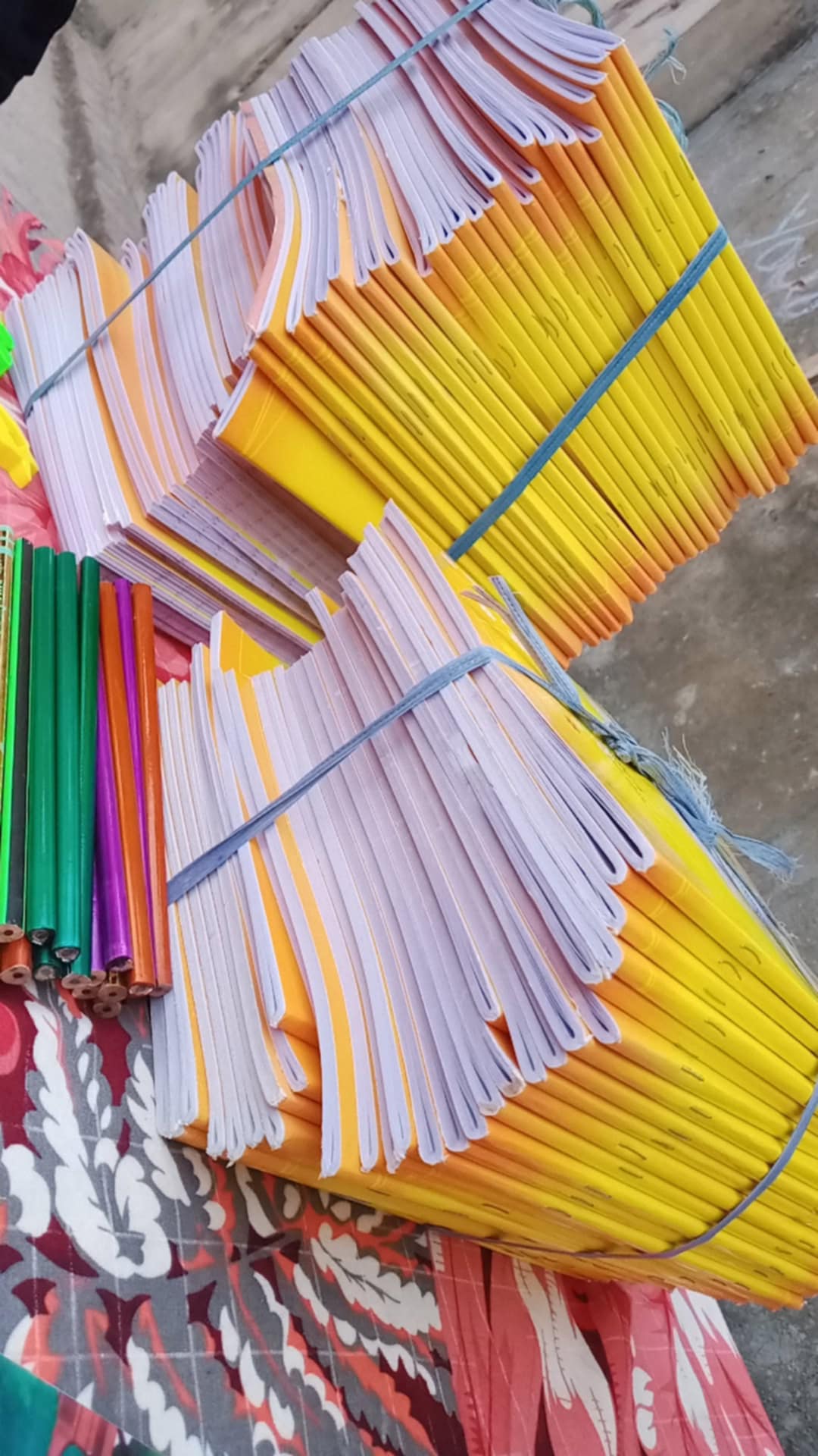 Bundles of yellow exercise books and colorful pencils.