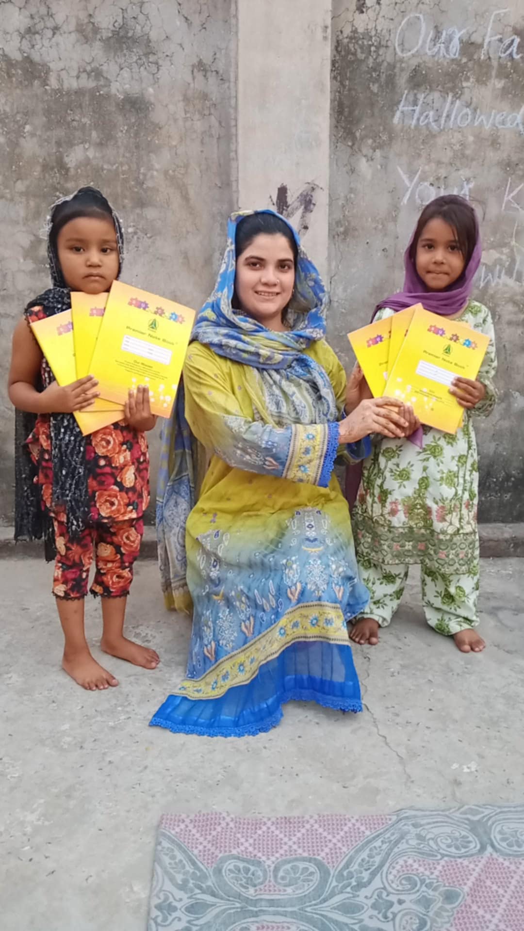 Two young girls and a volunteer holding yellow notebooks.