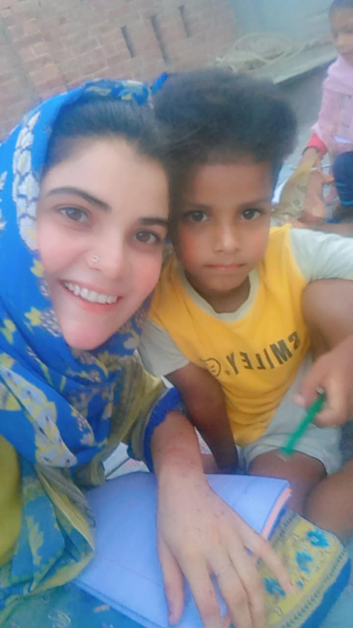 A volunteer smiling beside a child holding a notebook.